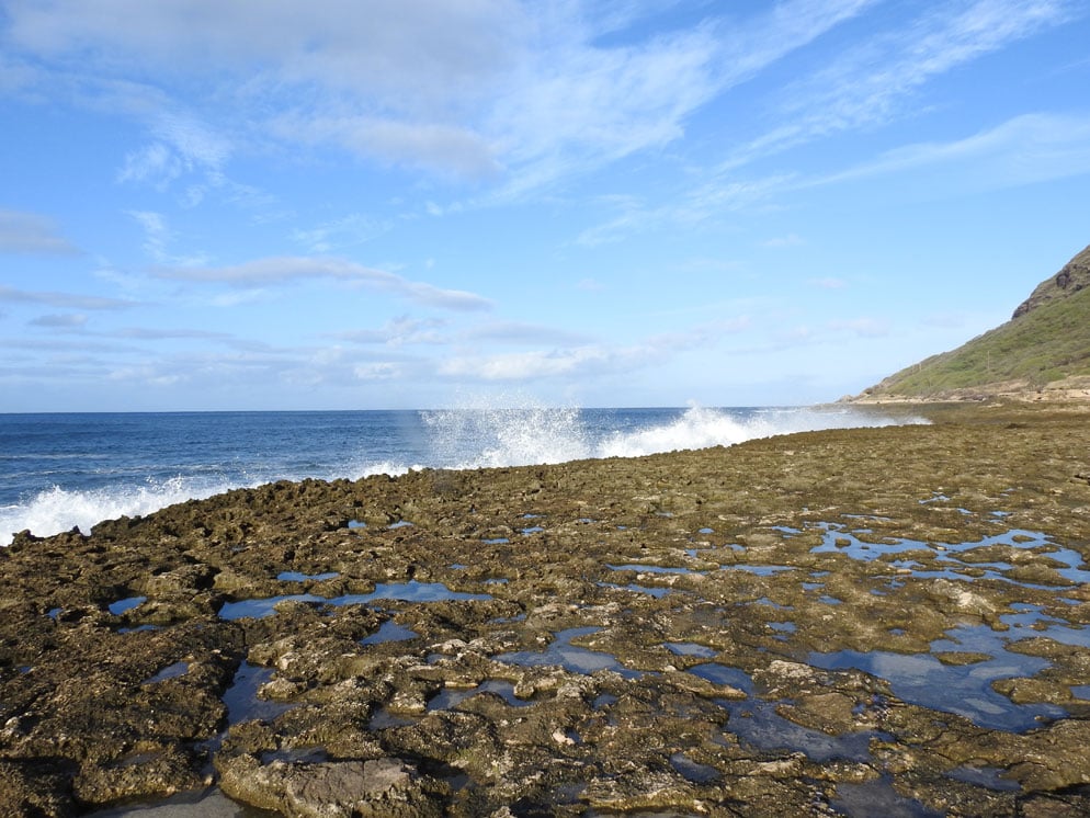 Zoom slider photo of a rocky shoreline with waves hitting it and a blue sky, wide shot