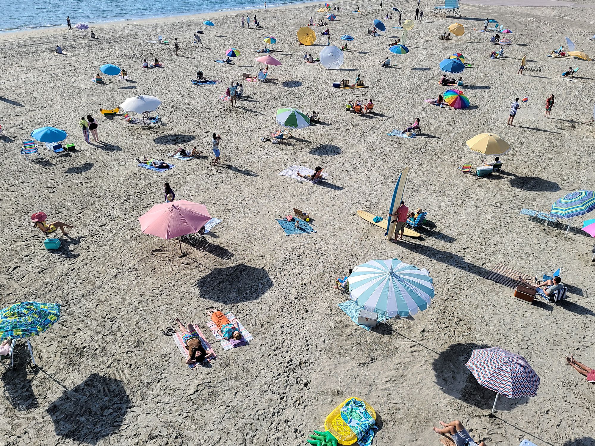 Photo taken on Galaxy S20 Ultra of a beach with many people. As we zoom in on the photo, we see a funny moment of a dog sitting on a beach towel with pink goggles on, showing how Space Zoom lets you find moments you might have otherwise missed