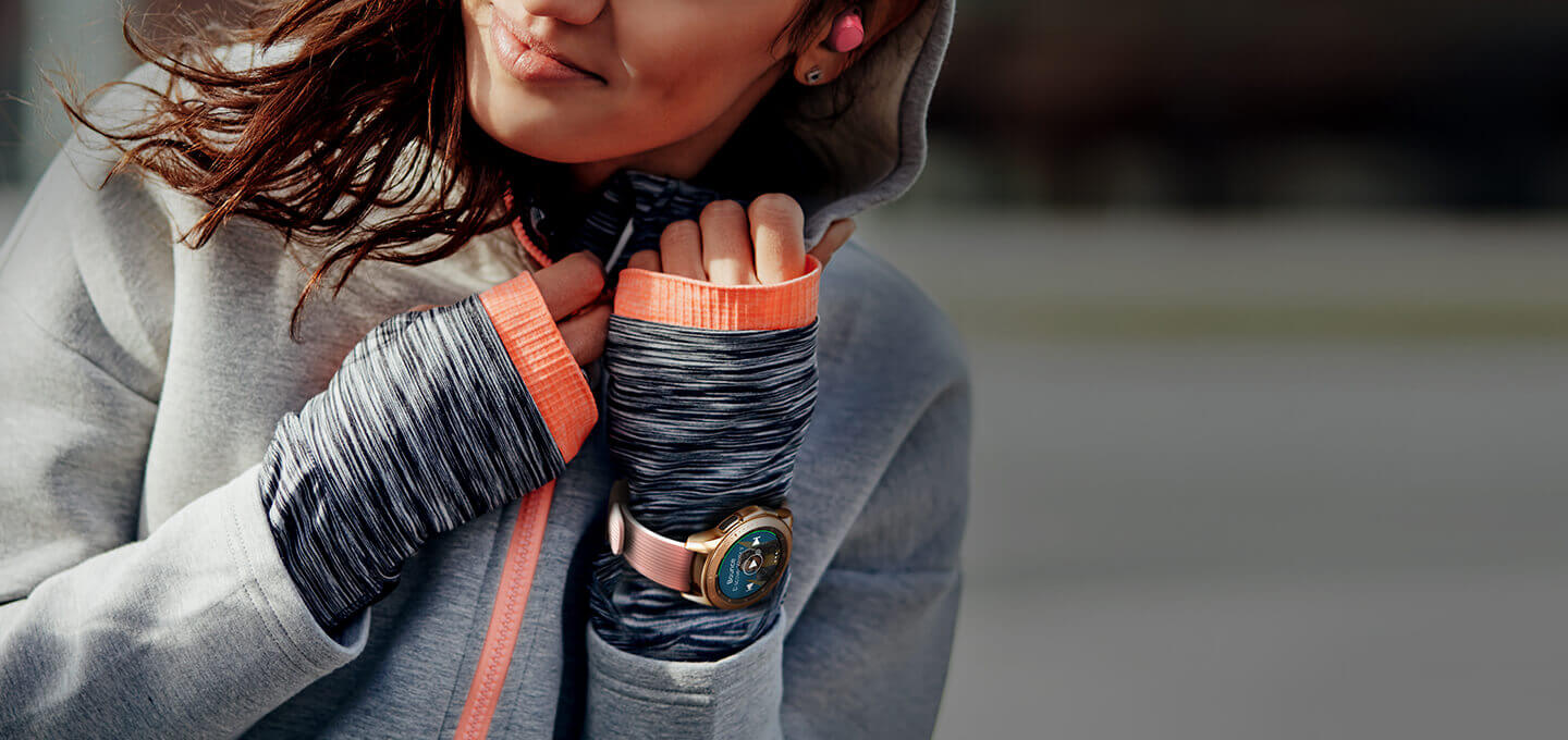 A woman in grey and orange jogging gear on a run wearing a 42mm Rose Gold  Galaxy Watch and pink Icon X earbuds.